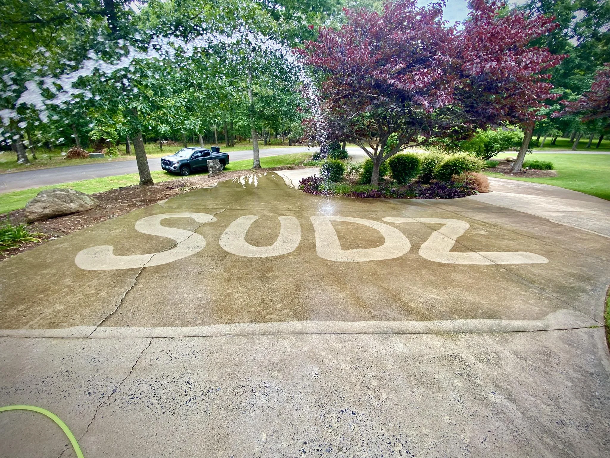 A driveway where SUDZ pressure-washed its name into the concrete, the clean letters bright against the darker surface.